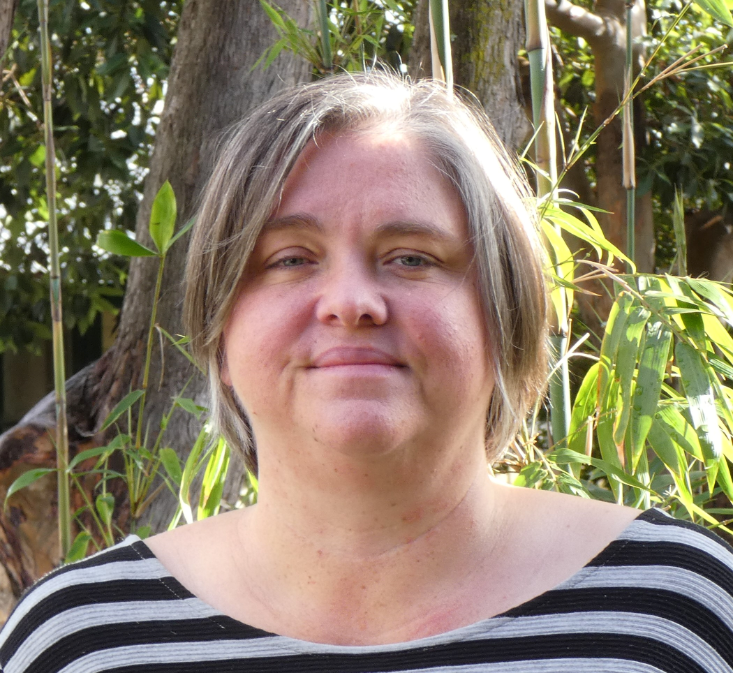 Headshot of Sarah Stokely, who has a light haired bobbed haircut and a grey and black striped top.