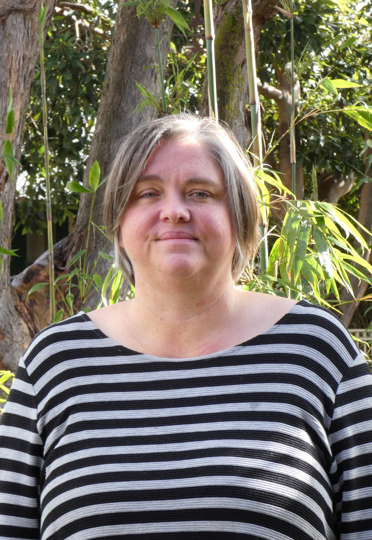 Headshot of Sarah Stokely, who has a light haired bobbed haircut and a grey and black striped top.